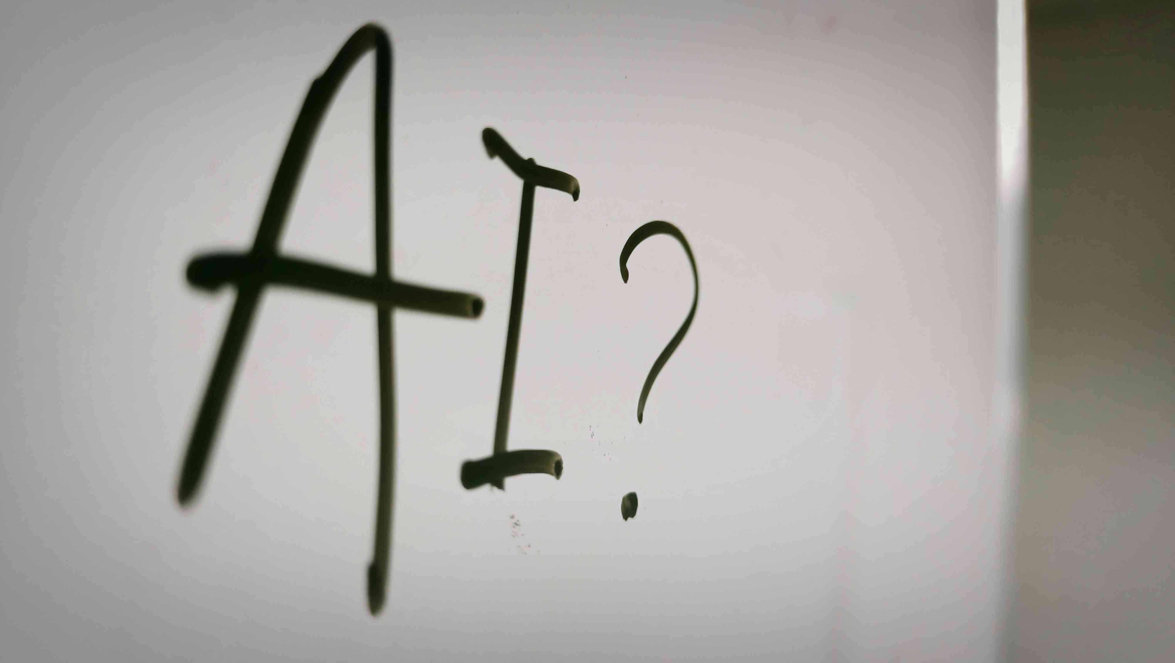 The letters AI and a question mark written in black marker on a whiteboard